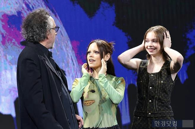 Tim Burton Wednesday Squid Game comparisonthree' '' 'im' '' 'urton' 'hand' 'gestures' 'smiles' 'blue' 'background.