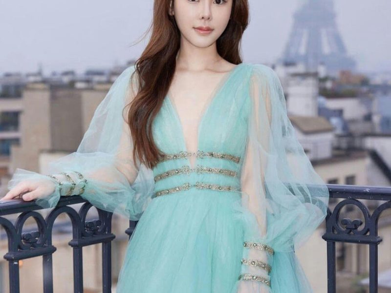 people-A-woman in a gown-A-Eiffel Tower in background-A-outdoor balcony setting-A-long flowing sleeves