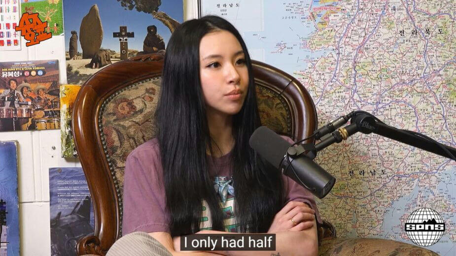 people-A-woman-A-long dark hair-A-seated-A-podcast interview-B-microphone-B-Korean map background-C-subtitle 