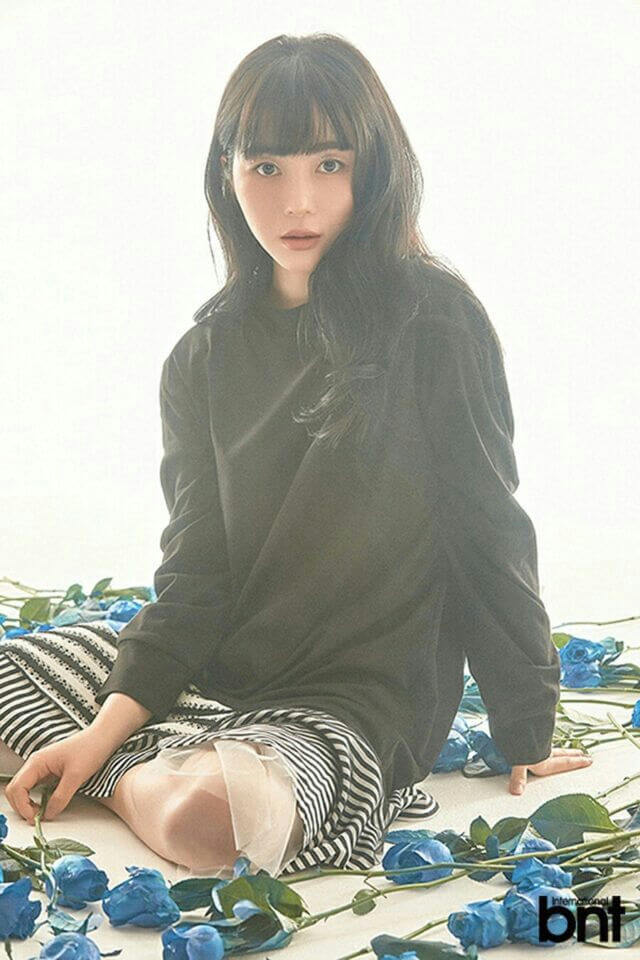 people-A-woman-A-dark hair-A-bangs-A-black shirt-A-striped skirt-A-blue roses-A-sitting on floor