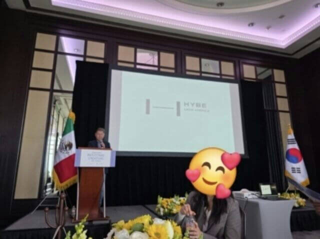 people-A-man speaking at podium-B-woman with emoji covering face-C-Mexican flag and South Korean flag present