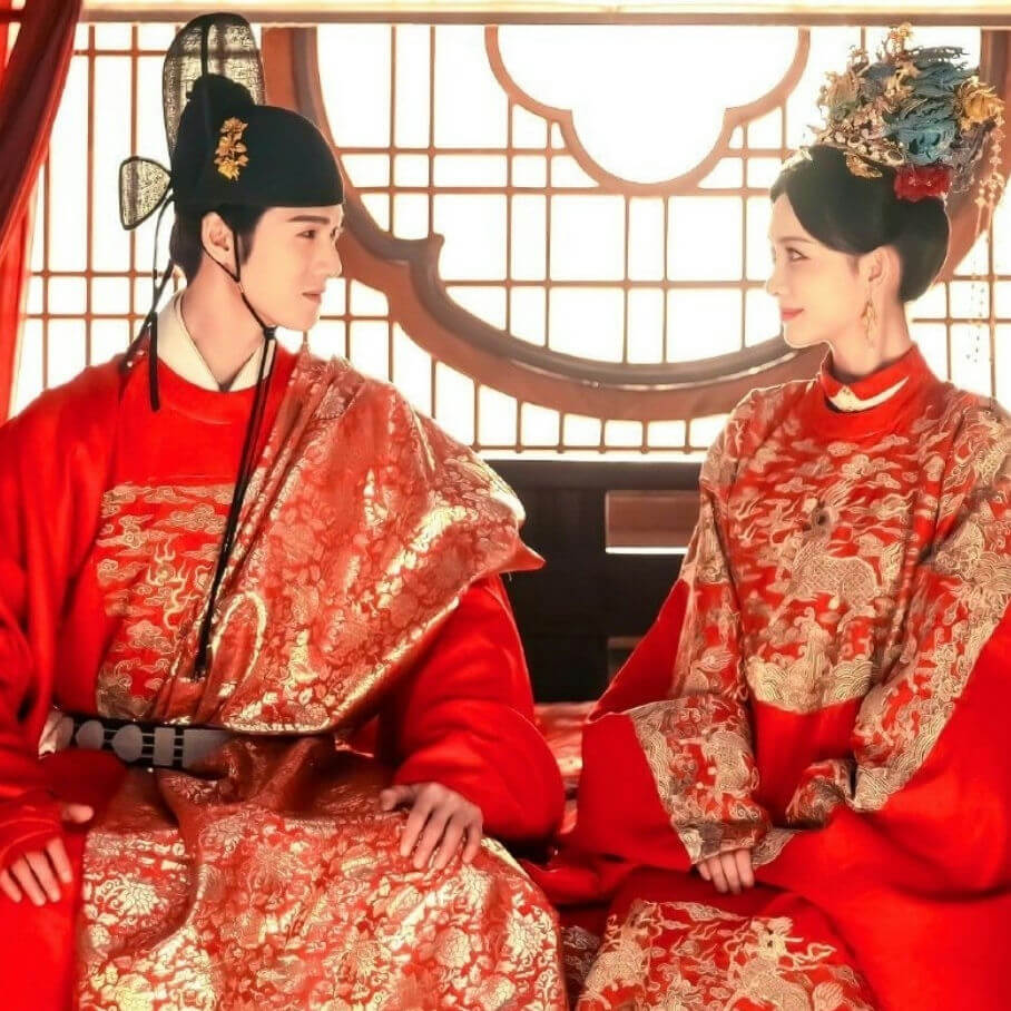 people-Two Asian individuals-A-traditional Chinese attire-A-red and gold brocade-B-wedding or royal setting-B-looking at each other-C-backlit window