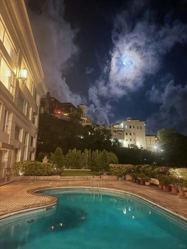 night-A-poolside-A-moonlit-sky-A-building-on-a-hill-A-swimming-pool