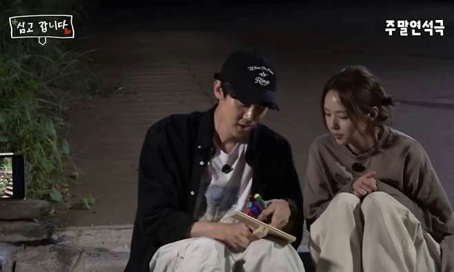 people-Two people-A-sitting outdoors at night-A-holding a small wooden object with colorful items-B-woman looking down-C-Korean text overlays