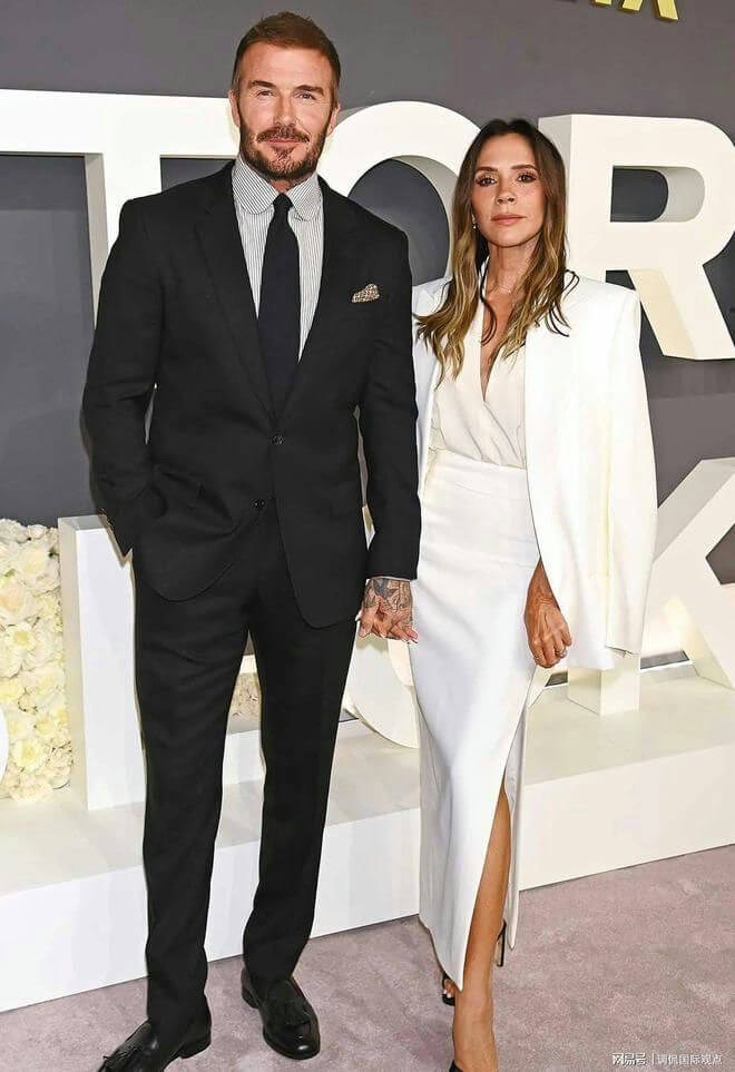 people-David Beckham-A-formal wear-A-black suit-A-striped shirt-A-tie-B-Victoria Beckham-B-white outfit-B-long white skirt-B-white blazer-C-holding hands-C-red carpet event