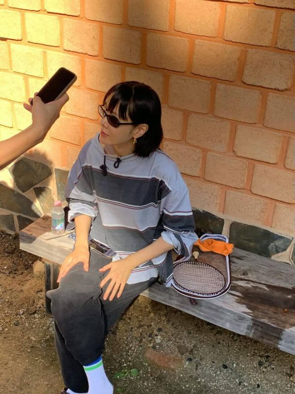 people-One woman-A-sitting-A-outdoor setting-A-brick wall background-A-sunglasses-B-striped shirt-C