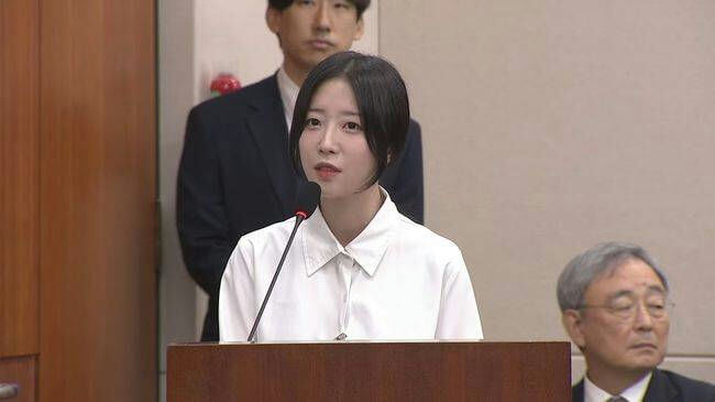 people-young woman speaking at podium-A-man standing behind her-B-older man seated in foreground-C-indoor setting