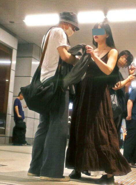 people-man in white shirt and mask-A-woman in long dark dress-A-man holding dark fabric-A-dark tote bag-A-indoor public space