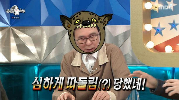people-One man-A-wearing a hyena-like mask-B-sitting at a table on a TV show set-C-Korean subtitles below him