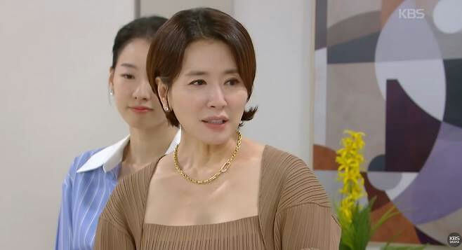 people-woman in foreground-middle-aged-woman in background-young-brown top and gold necklace-blue and white striped shirt-KBS logo