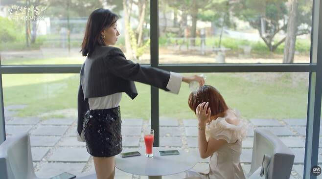 people-woman in dark cropped blazer and sequined mini-skirt-A-pouring liquid over head-B-woman in light ruffled dress covering face-C-indoor setting with large windows overlooking greenery