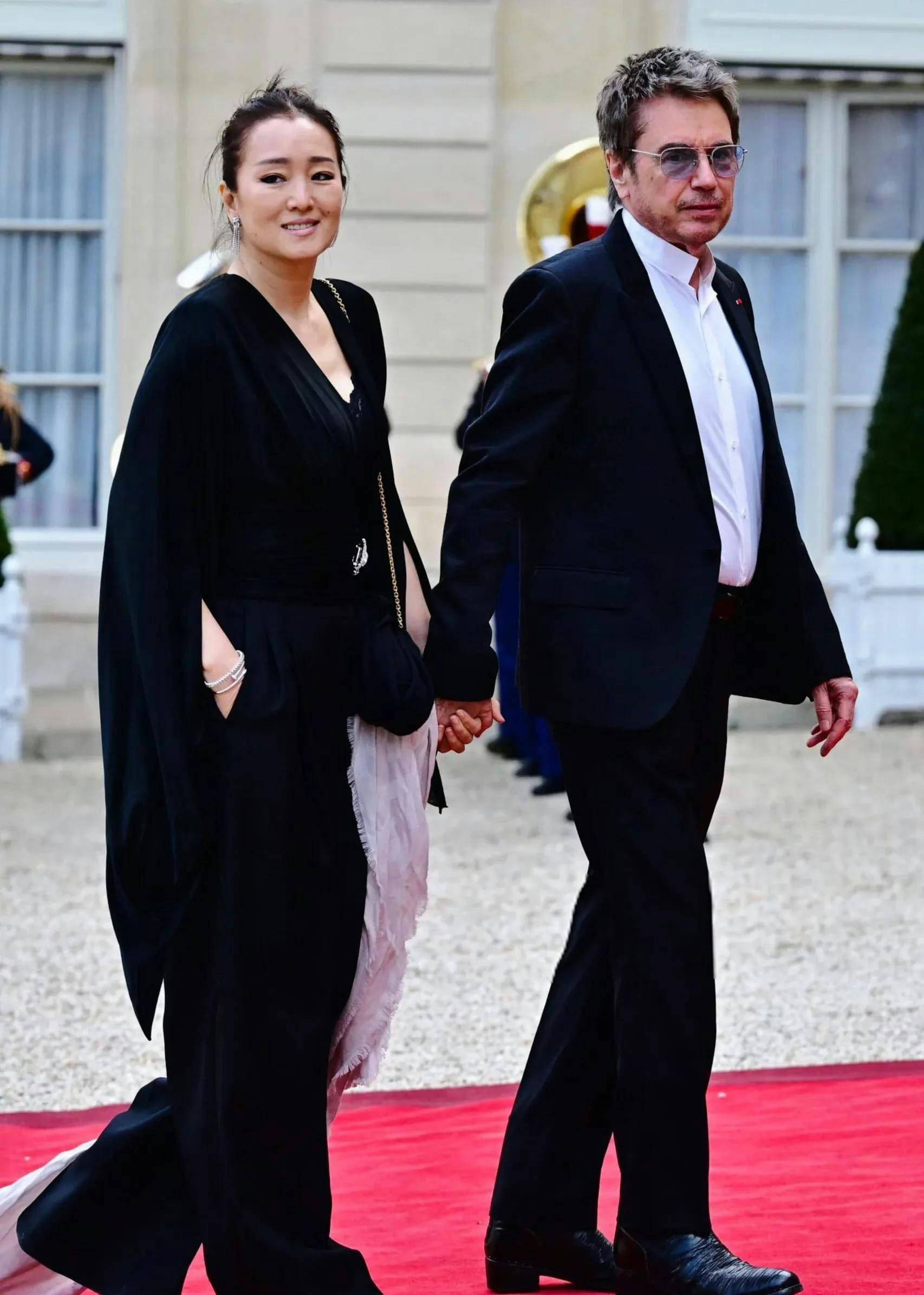 people-A-woman in black dress-A-man in suit-A-holding hands-A-walking on red carpet