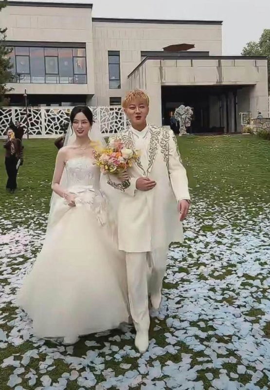 people-A-bride and groom-A-walking down aisle-B-white wedding attire-C-flower petals on grass