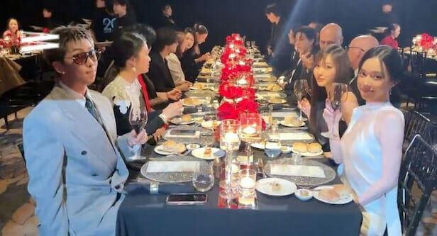 people-Man in light suit and sunglasses-A-Formal dinner-A-Long dining table-B-Red floral centerpiece-C-Woman in white dress holding wine glass