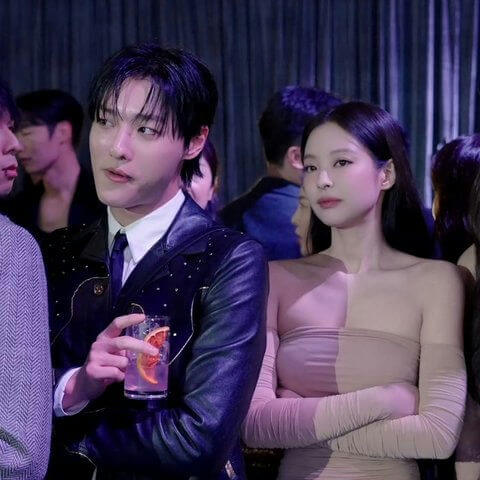 people-Two main figures-A-man in black leather jacket-A-woman in strapless beige dress-A-holding drink-B-black hair-B-arms crossed-C-party setting-C