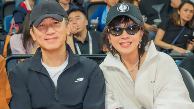 people-two people sitting side-by-side in an audience-A-man wearing a black baseball cap and black jacket-A-woman wearing a black baseball cap with a