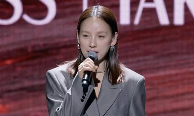 people-woman-singing-A-microphone-A-gray blazer-A-hoop earrings-A-long brown hair