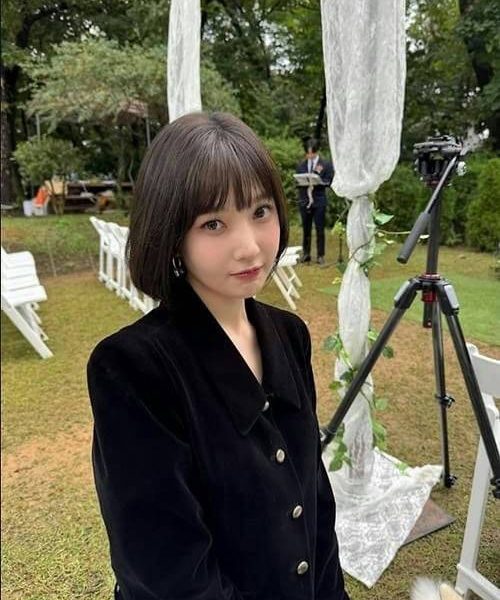 people-woman-short black hair-outerwear-black jacket-setting-outdoor wedding setup-object-camera on tripod