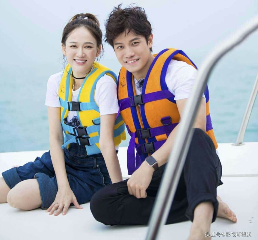 people-A-smiling woman-A-yellow and blue life vest-B-smiling man-B-orange and purple life vest-C-sitting on a boat deck with water background