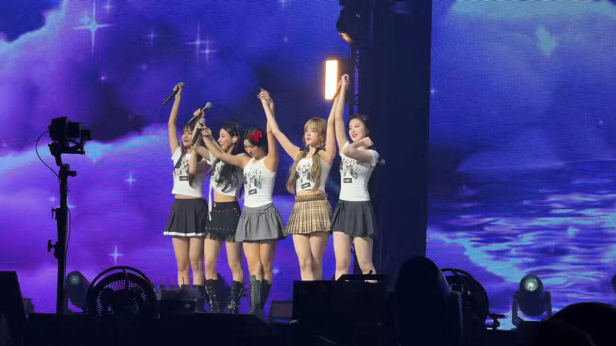 people-5 female performers-A-stage-A-holding microphones-B-raising arms-B-purple/blue lighting-C-skirt outfits-C