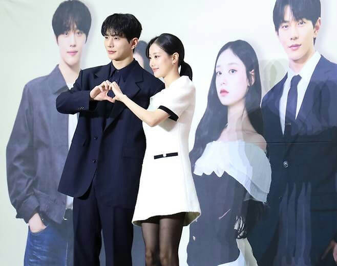 people-Two people posing in front of a backdrop-Two people posing in front of a backdrop-Man in dark suit-Woman in white dress-Heart gesture with hands