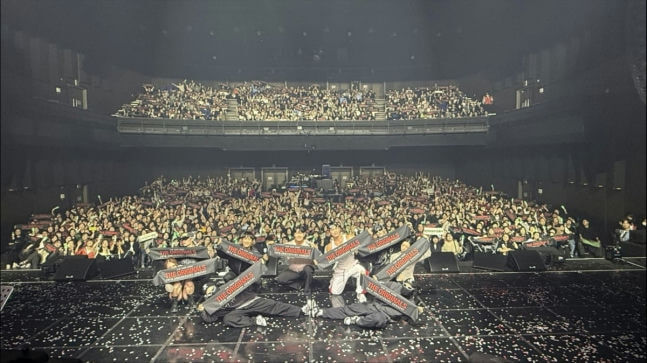 people-group on stage holding banners-audience in auditorium-concert setting-confetti on floor