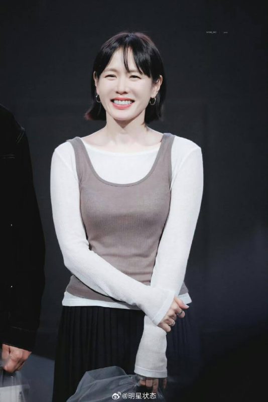 people-Korean actress Son Ye-jin-A-smiling-A-short black hair-A-wearing layers of a white long-sleeve shirt and a brown tank top-A-dark background