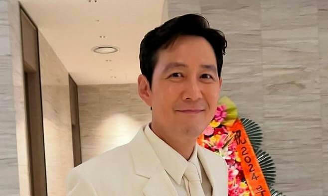 people-Lee Jung Jae-smiling-in a white suit-in front of a floral arrangement-indoors