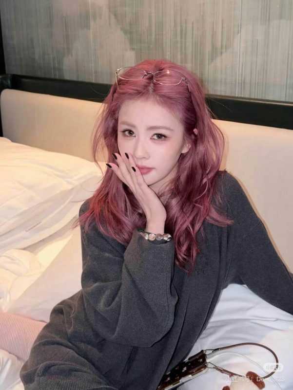 people-A-woman-A-pink hair-A-dark gray sweater-A-holding hand to mouth