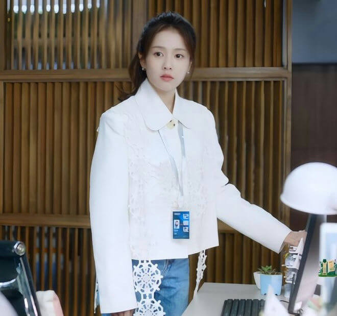 people-A-woman-A-white cropped jacket-A-lace detailing-A-ID badge-A-blue jeans-A-indoor office setting
