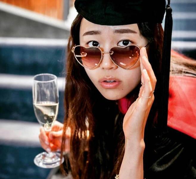 people-woman-graduation cap-holding champagne flute-heart-shaped sunglasses-gold bracelet