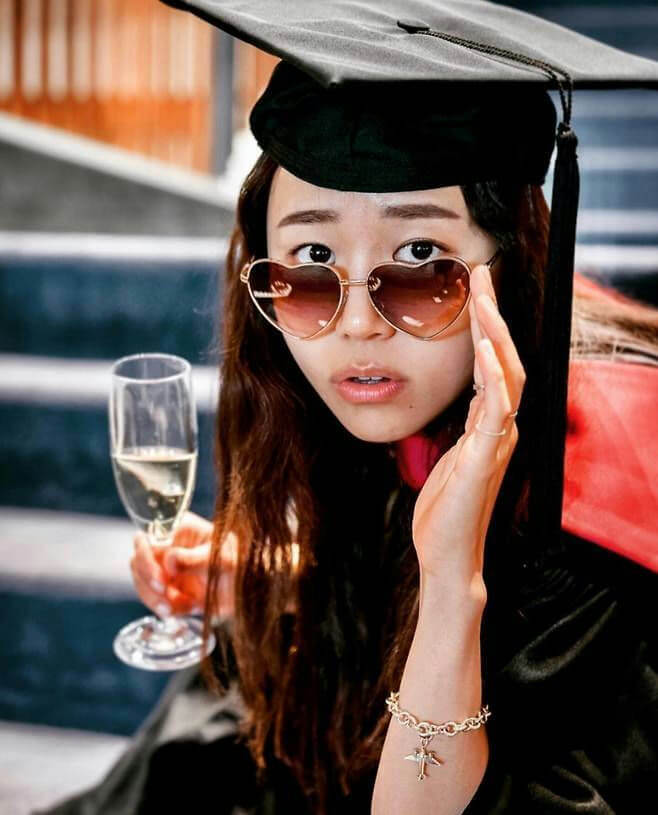 people-woman-graduation cap-holding champagne flute-heart-shaped sunglasses-gold bracelet