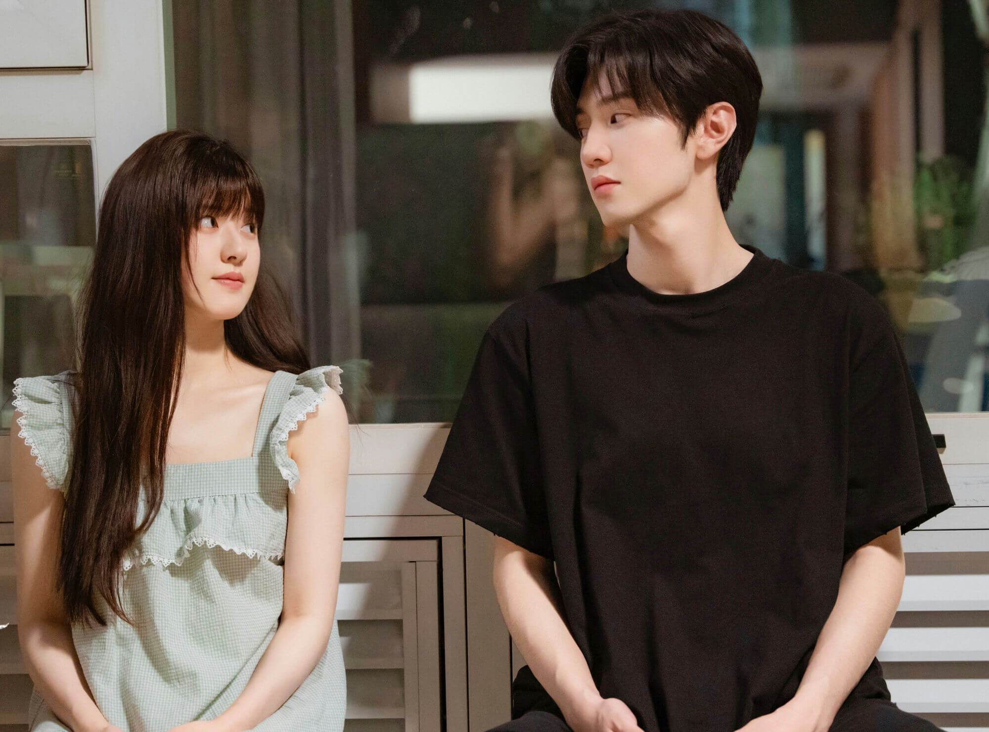 people-two young Asian individuals-A-sitting close together-B-soft lighting-C-intimate moment