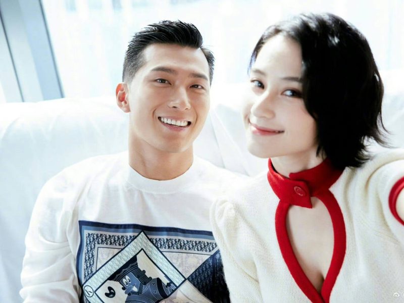 people-Two people (a man and a woman)-A-smiling-A-man with dark, slicked-back hair-B-woman with short, dark hair wearing white and red clothing-C-brightly lit indoor setting with white background