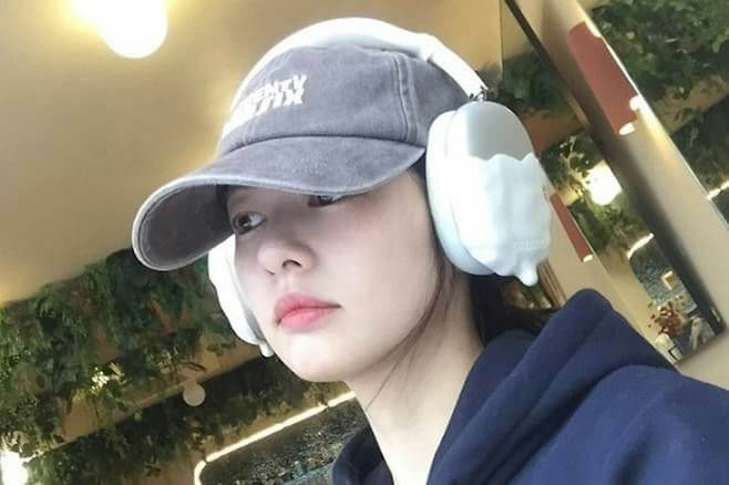people-young woman-A-wearing headphones-A-wearing baseball cap-A-casual outfit-A-selfie-A-indoor setting