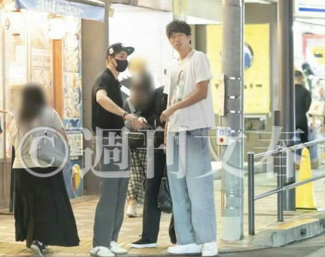 people-Three people outdoors, two men and one woman, one man wearing a white T-shirt and light blue wide-leg jeans, the other man wearing a black shirt and black cap, the woman wearing a light top and black long skirt, next to a light pole on a city street-tall man-casual attire-masked man