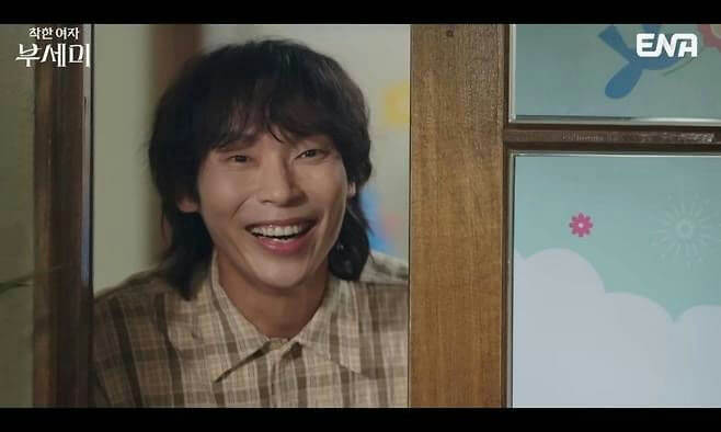 people-A-man smiling broadly-A-plaid shirt-B-peeking from behind a door frame-C-ENA logo visible