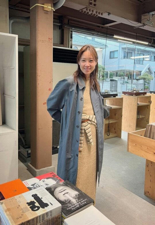 people-1-woman-A-smiling-A-long-blue-trench-coat-A-standing-indoors-A-in-a-store