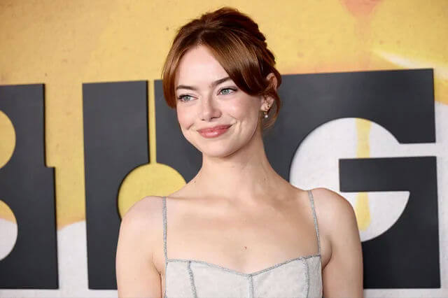people-Emma Stone-smiling-updo hairstyle-reddish brown hair-light gray spaghetti strap dress-event background