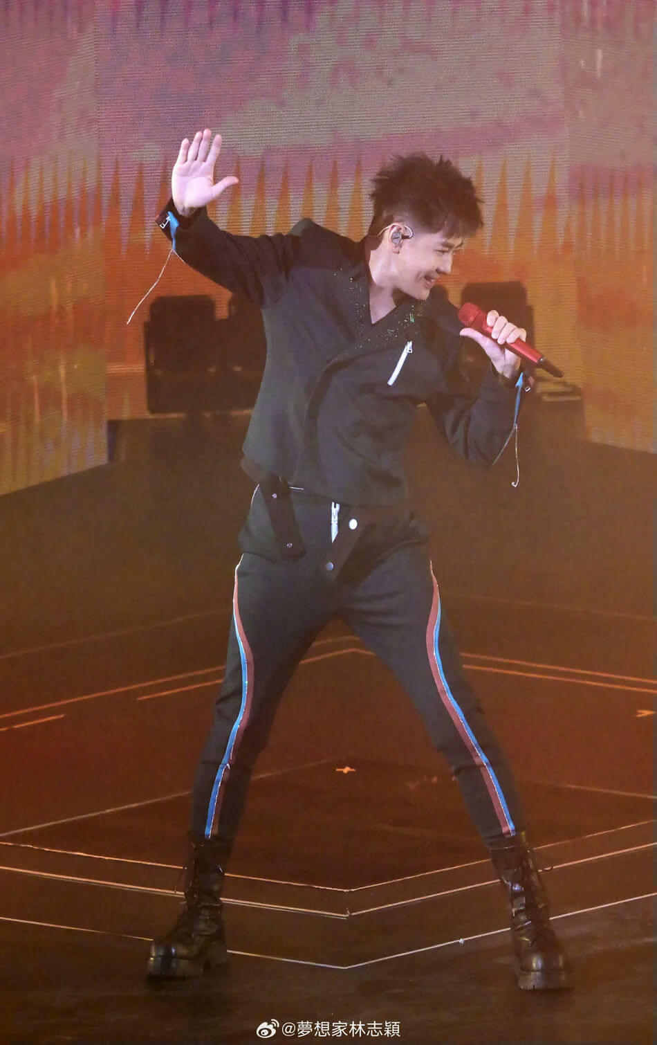 people-1-singer-A-on-stage-A-performing-A-holding-microphone-A-waving-hand-A-wearing-black-suit-A-wearing-platform-boots