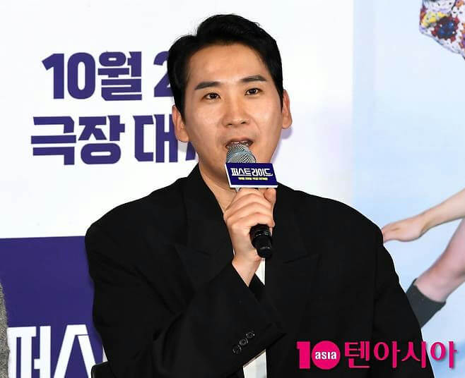 people-man-speaking into a microphone-wearing a black suit-at a promotional event-korean text visible
