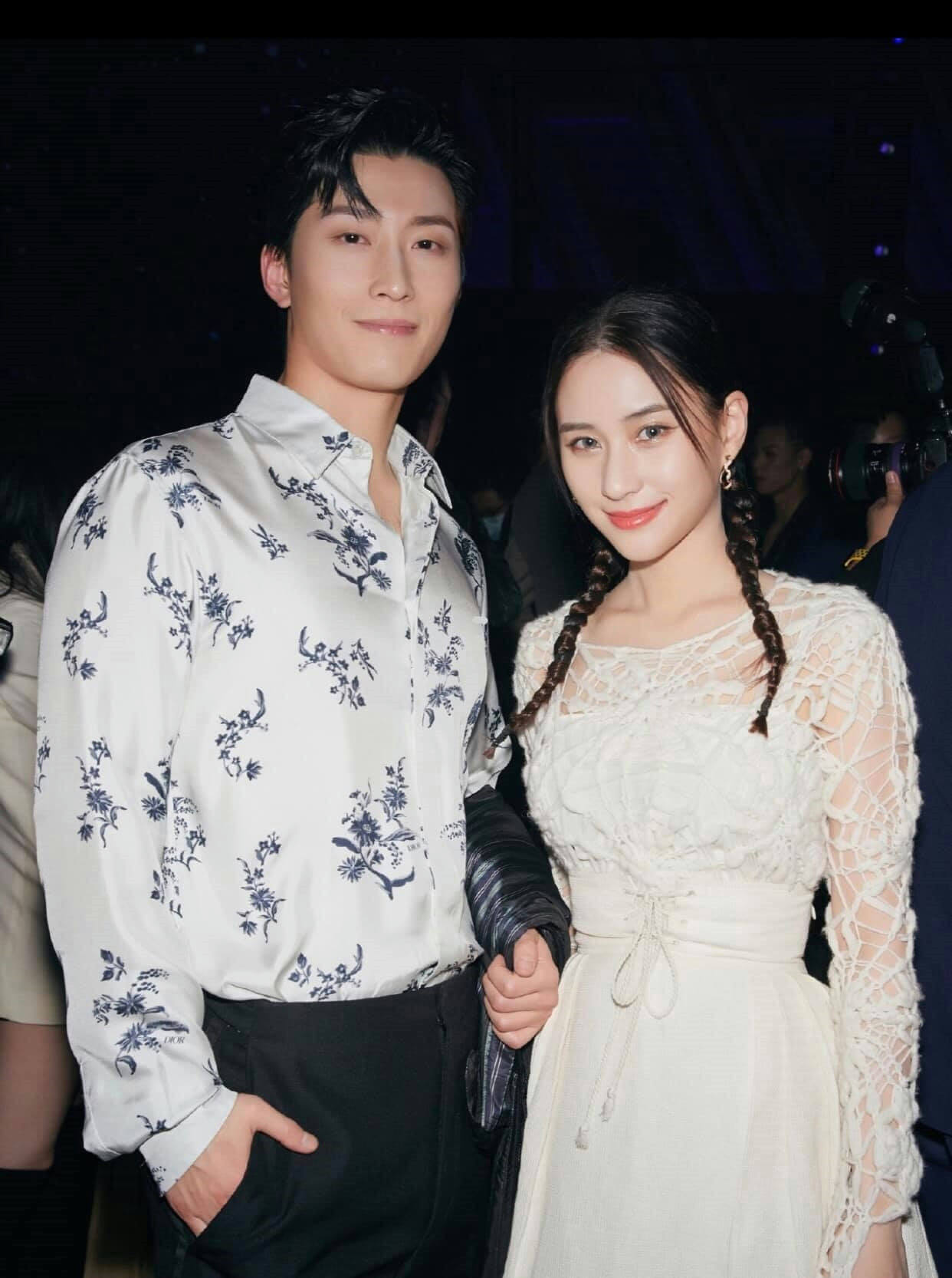 people-man and woman posing together-man wearing white and blue floral shirt and black pants-woman wearing white lace dress with braided pigtails-formal event setting