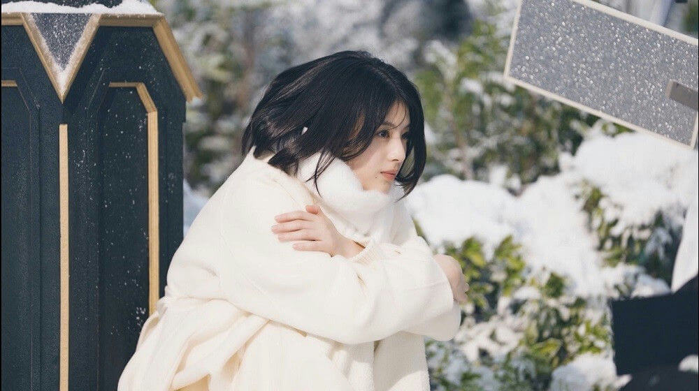 people-woman-A-short black hair-A-white coat-A-snowy outdoor setting-B-looking downcast-C-hugging herself
