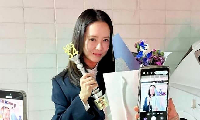 people-One woman-A-holding trophy-A-smiling-B-flowers-C-taking photo