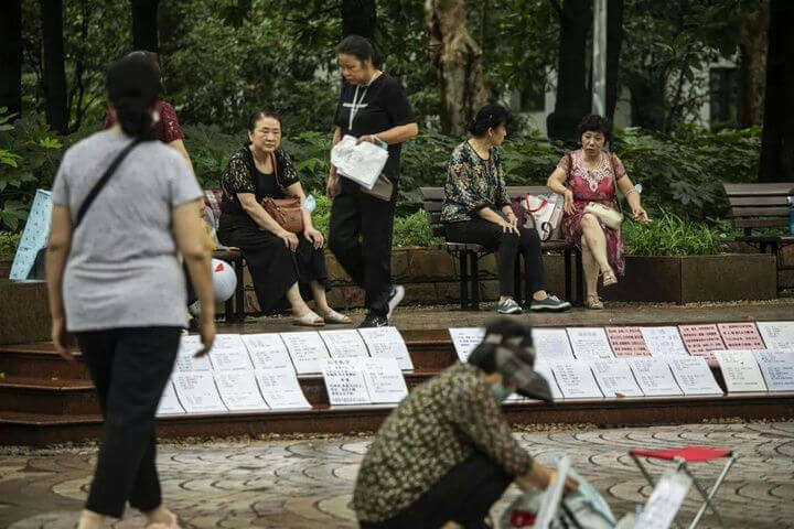 people-several Asian women-A-sitting on park benches-A-viewing posted notices-B-in a park setting-C