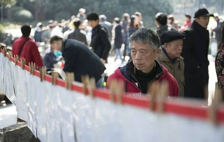 people-Man with gray hair in red jacket-A-Crowd in background-B-Papers hanging on line with clothespins-C