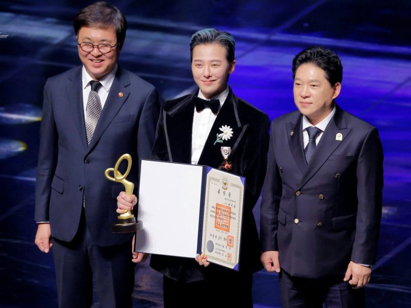 people-Three men-A-award ceremony-A-holding trophy-A-holding certificate-B-wearing formal attire-B-daisy lapel pin-C-blue lighting