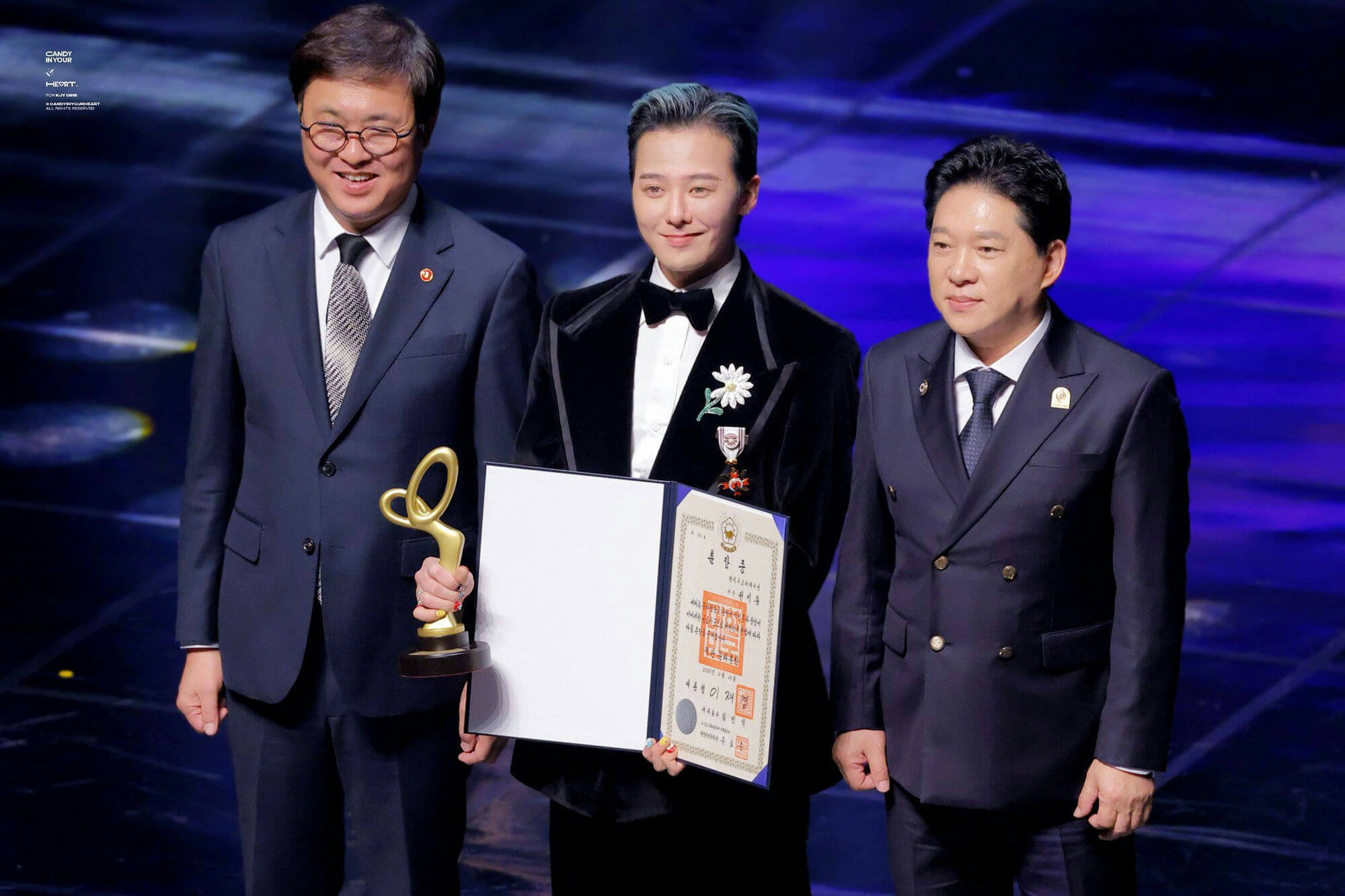 people-Three men-A-award ceremony-A-holding trophy-A-holding certificate-B-wearing formal attire-B-daisy lapel pin-C-blue lighting
