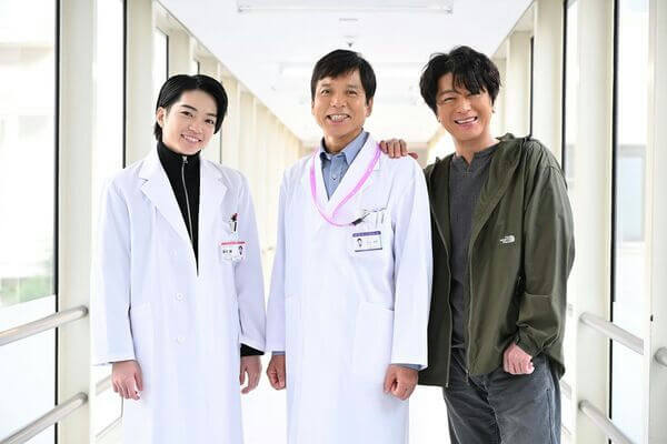 people-three men-A-hospital hallway-A-two in white lab coats-B-one in casual jacket-C-smiling