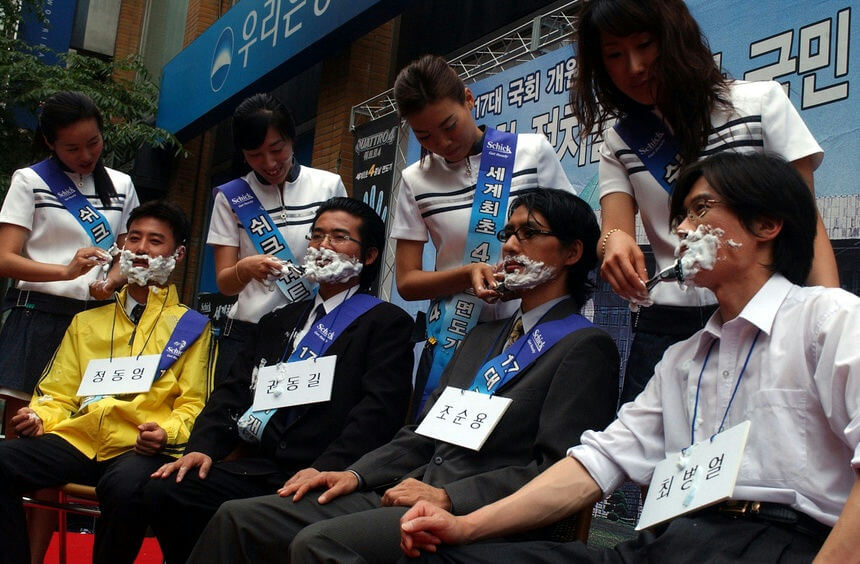 people-four men with shaving cream on their faces being shaved-four women applying shaving cream and shaving-promotional event-Korean text visible-Schick branding visible